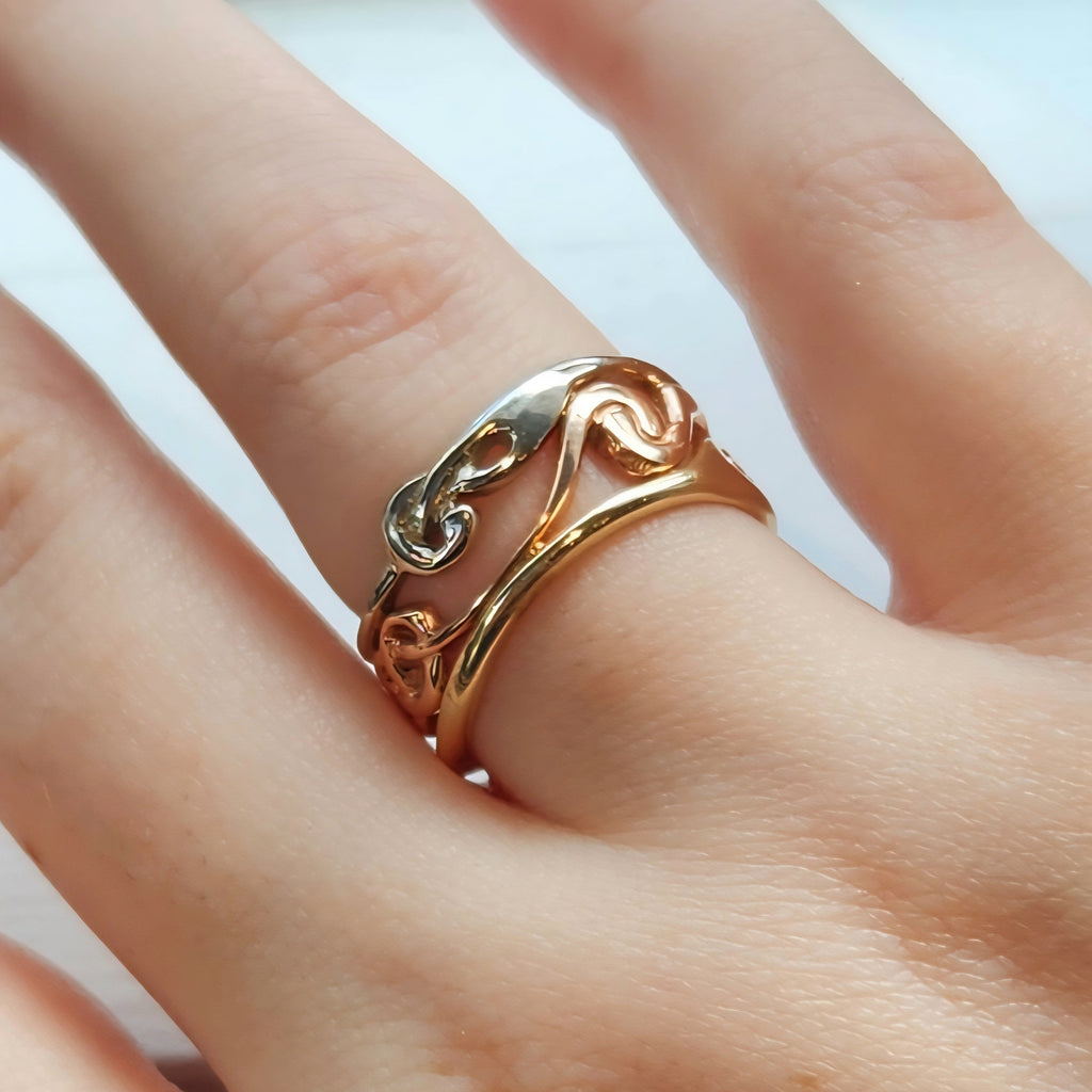 Gold ring with a wavy design on a person's finger against a neutral background