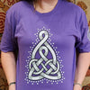 Person wearing a purple t-shirt with a white Celtic Mother's knot design on a patterned carpet background