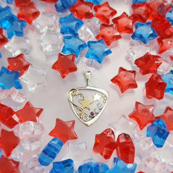A Sterling Silver Downward facing Triangular Frame with two 14 Karat Yellow Gold alternating Stars in the center.  Silver and a Gold Double Swirl accenting the Right side of the pendant.  Evenly placed around the frame, are some 14 Karat Yellow Gold Beads. On the left side there are a bezel set Sapphire, Diamond and Ruby. In that order. To symbolize the colors of the American Flag. This pendant is called The Liberty Star Pendant & was made by our Craftsman Sydney. This pendant includes an 18" Cable Chain.