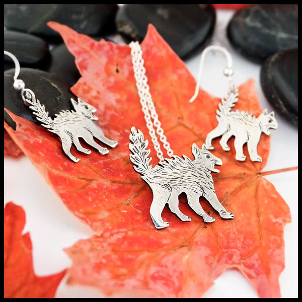Silver Scaredy Cat necklace and earrings on red leaves with black stones in the background