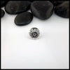 Silver flower-shaped Sterling Silver Pin on a white surface with black stones in the background