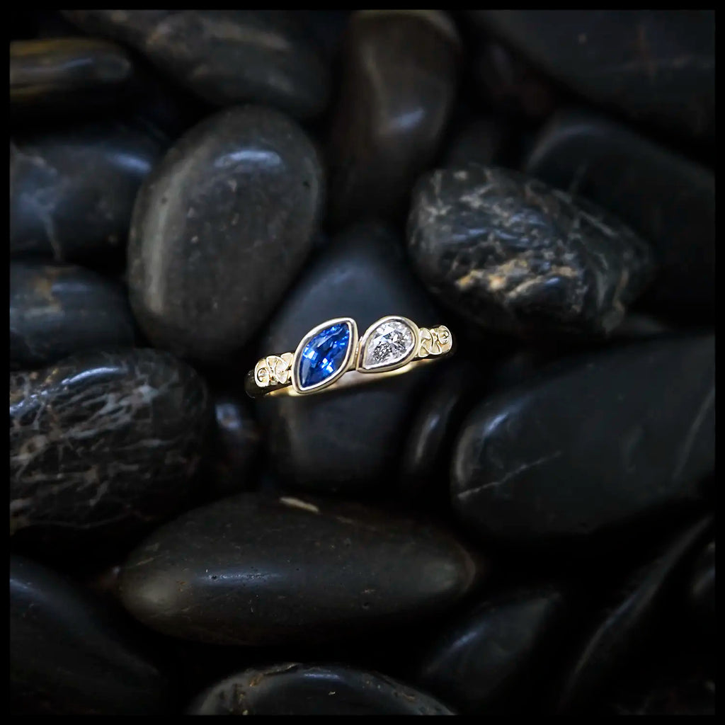 14K Yellow Trinity Scroll ring with a blue sapphire Marquise and diamond pear set on black pebbles