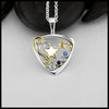 A Sterling Silver Downward facing Triangular Frame with two 14 Karat Yellow Gold alternating Stars in the center.  Silver and a Gold Double Swirl accenting the Right side of the pendant.  Evenly placed around the frame, are some 14 Karat Yellow Gold Beads. On the left side there are a bezel set Sapphire, Diamond and Ruby. In that order. To symbolize the colors of the American Flag. This pendant is called The Liberty Star Pendant & was made by our Craftsman Sydney. This pendant includes an 18" Cable Chain.