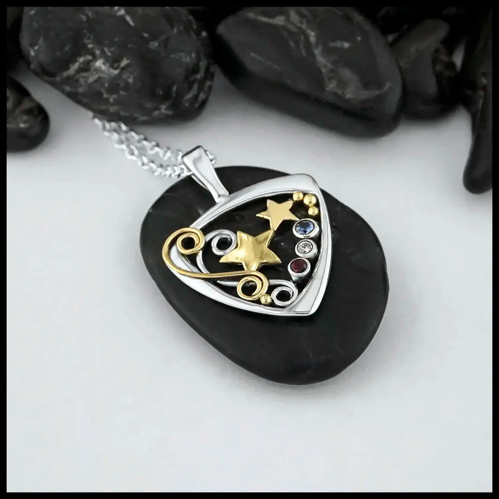 A Sterling Silver Downward facing Triangular Frame with two 14 Karat Yellow Gold alternating Stars in the center.  Silver and a Gold Double Swirl accenting the Right side of the pendant.  Evenly placed around the frame, are some 14 Karat Yellow Gold Beads. On the left side there are a bezel set Sapphire, Diamond and Ruby. In that order. To symbolize the colors of the American Flag. This pendant is called The Liberty Star Pendant & was made by our Craftsman Sydney. This pendant includes an 18" Cable Chain.