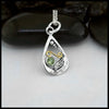 A small Tear Drop Frame in Sterling Silver. In the lower left is a Sterling Silver Feather charm, adjacent to the feather is a bezel set Peridot. Immediately above lies an 18 Karat Yellow Gold Spiral. Lastly there are three descending Sterling Silver beads on the inner top left of the frame. This pendant includes an 18" Cable Chain. Made by Sydney.