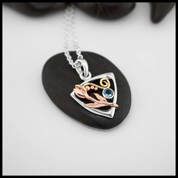 The latest necklace from out Craftsman Nicole! A Sterling Silver Triangular Frame Pendant with a 14K Yellow Gold Swirl accenting the top, a 14K Rose Gold Tulip & beading on the right side adjacent to a bezel set Aquamarine on the left. Includes an 18" Cable Chain 
