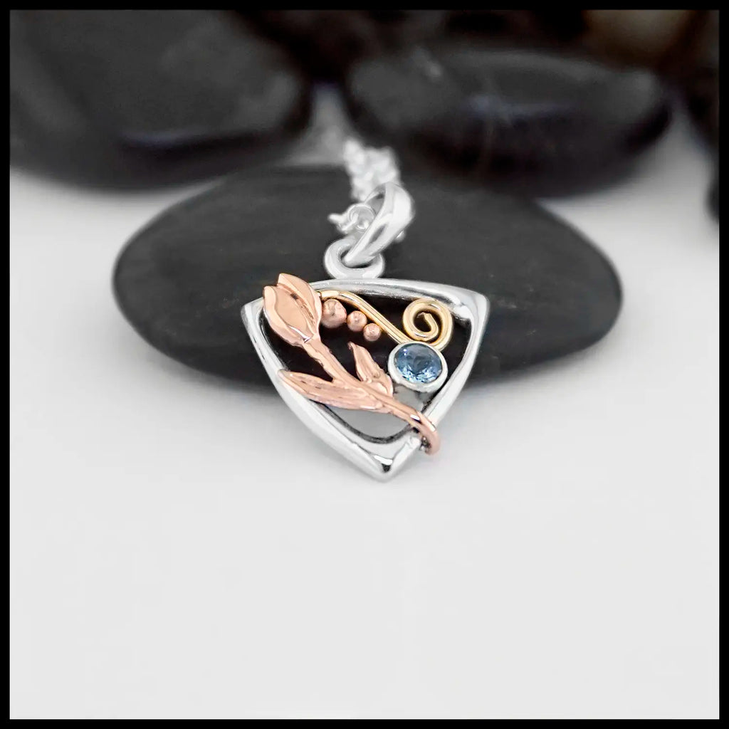 Sterling Silver Triangular Frame Pendant with a 14K Yellow Gold Swirl accenting the top, a 14K Rose Gold Tulip & beading on the right side adjacent to a bezel set Aquamarine on the left. Includes an 18" Cable Chain 