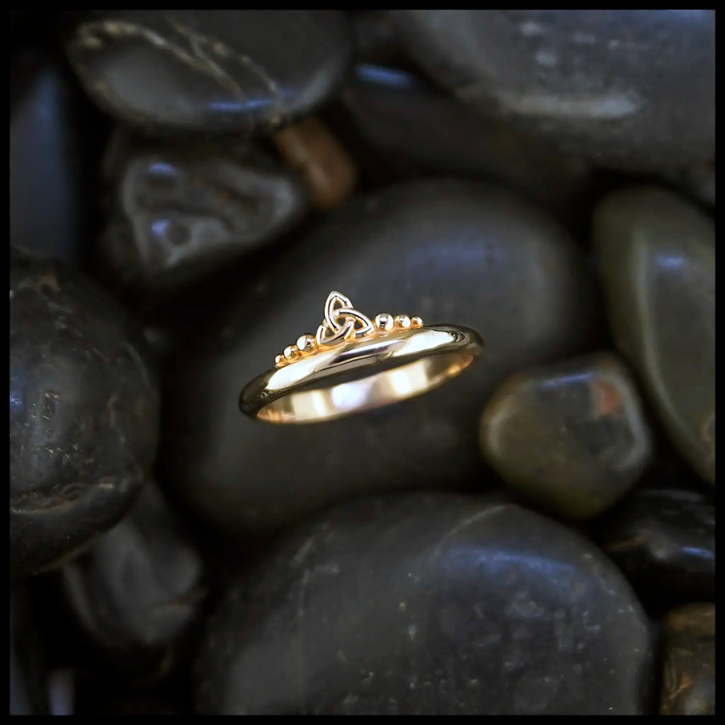 Gold ring with a trinity knot and beading design on dark stones