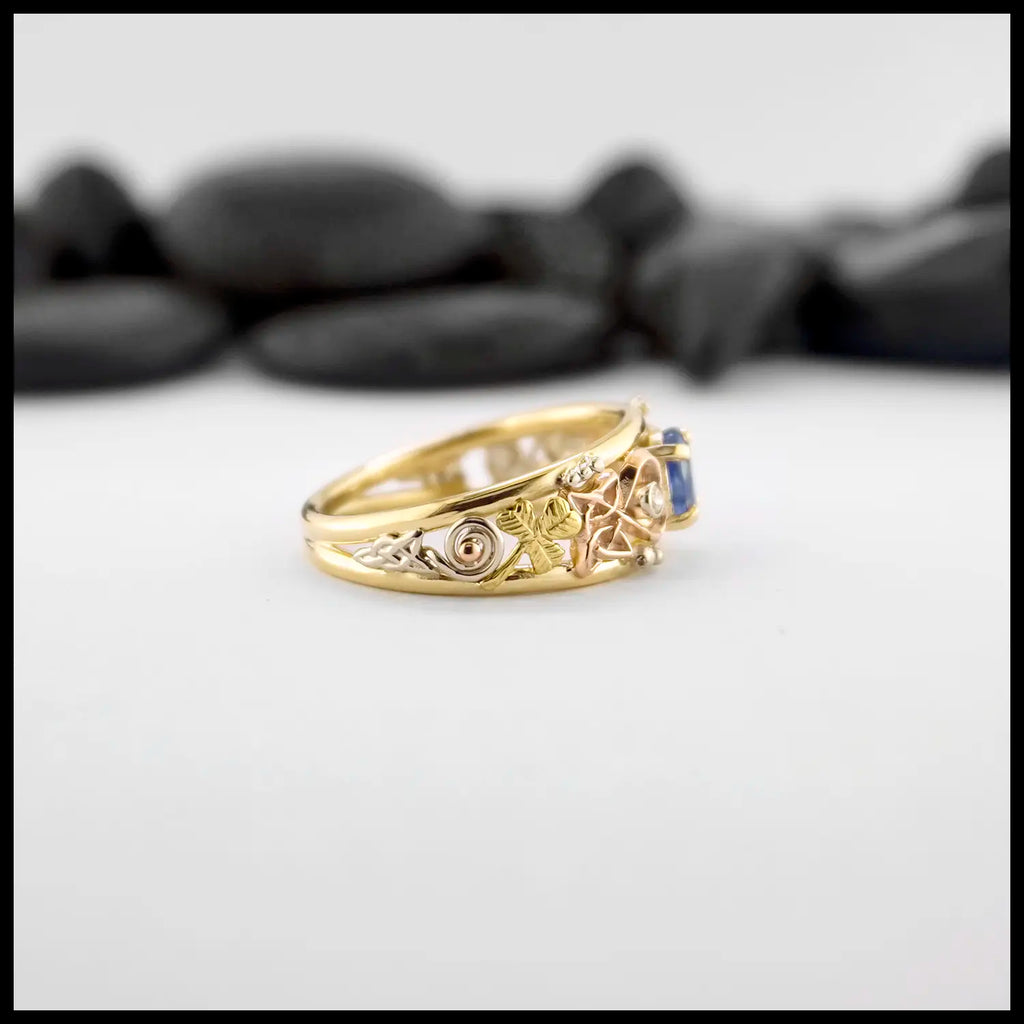 Gold custom frame ring with rose gold, white gold, and yellow gold set with two diamonds and an oval blue sapphire