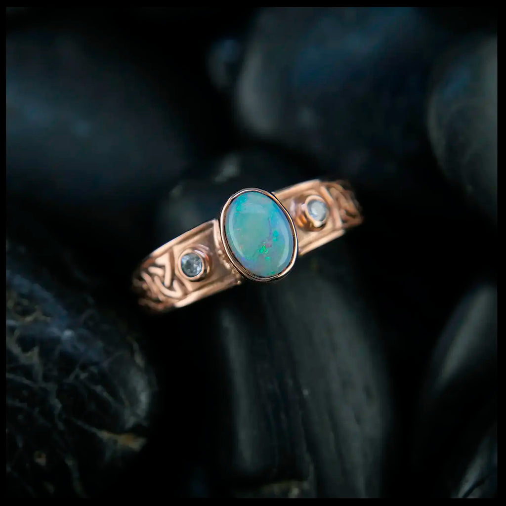 Rose gold ring with an opal and two diamonds on a dark background