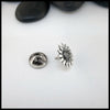 Silver flower-shaped Sterling Silver Pin on a white surface with black stones in the background