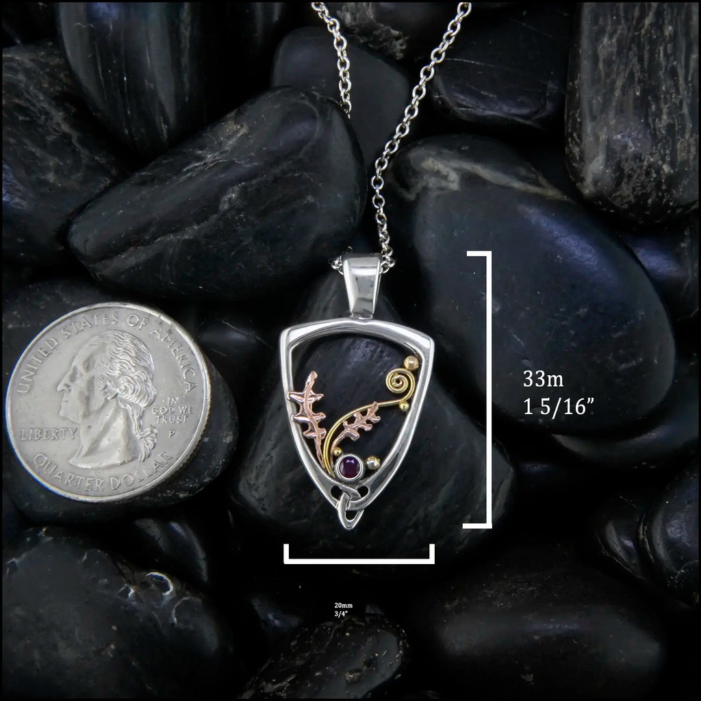 Silver Frame pendant with 14K rose gold oak leaves, 14K yellow gold spirals and beads. set with a 2mm ruby.
Measures at 33mm x 20mm