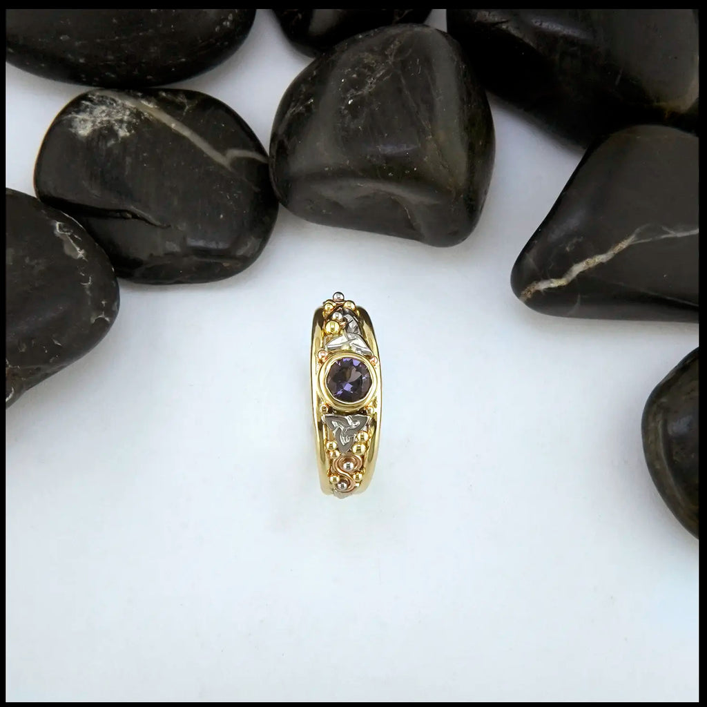Gold ring with purple spinel on a white background with black stones