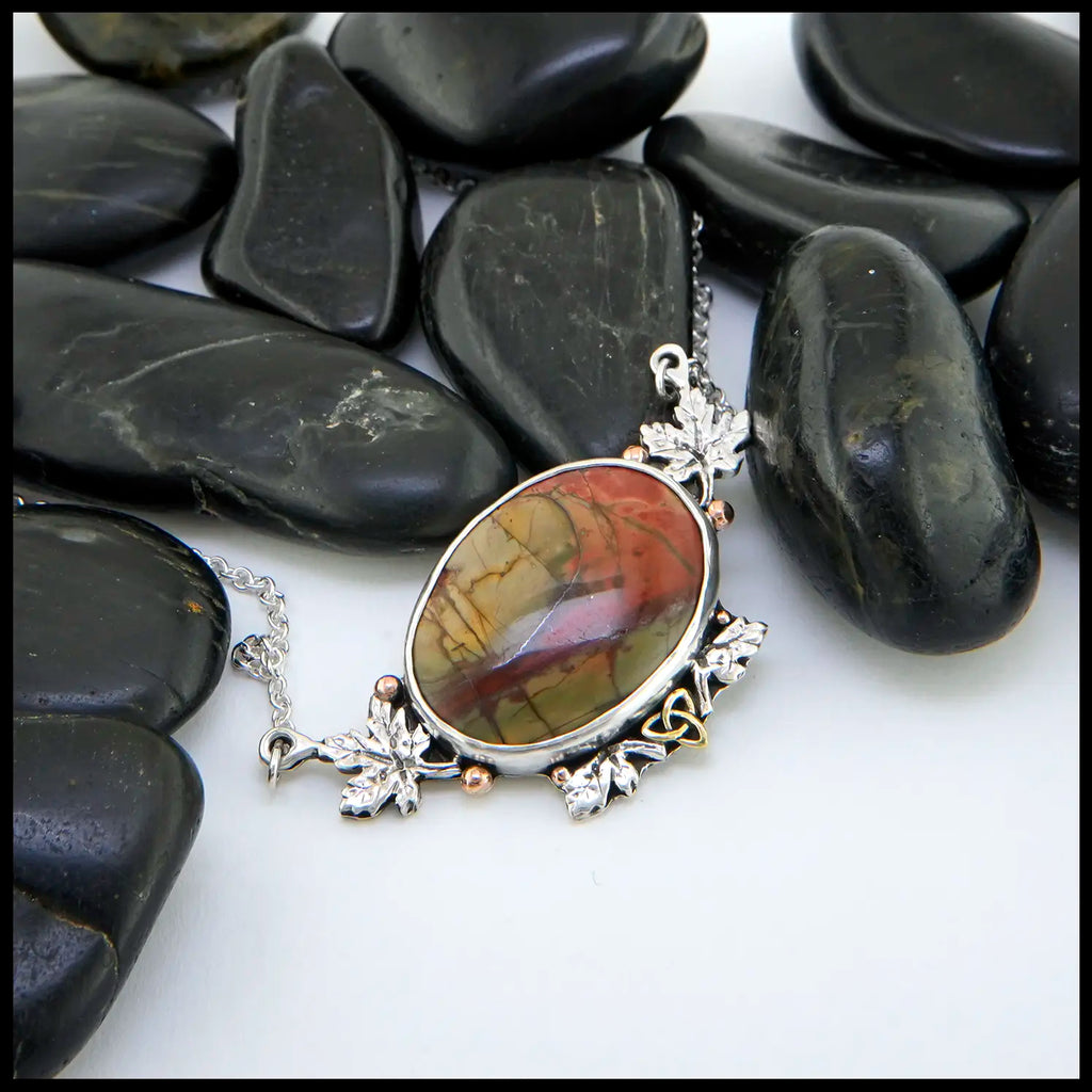 Red Creek Jasper set in Sterling Silver! surrounding the bezel are Sterling Silver maple leaves, 14K Rose Gold beads, and an 18K Yellow Gold Trinity.