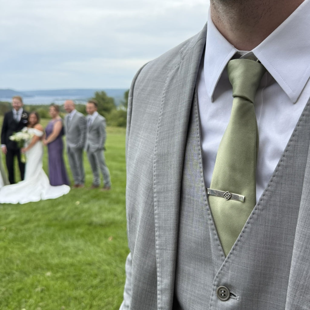 Celtic knot tie bar worn at a wedding, with the bride and groom in the background